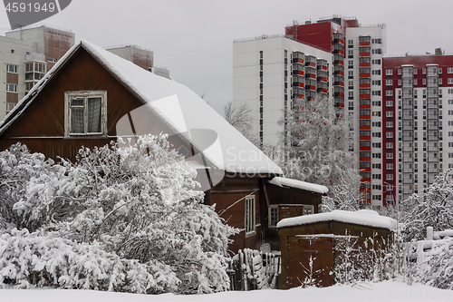 Image of Old wooden house against the background of new tall city houses in winter