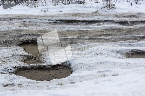 Image of Road with deep holes, water, ice and snow in Russian city in winter