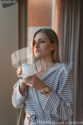 Image of young woman enjoying evening coffee by the window