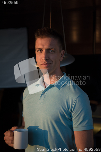 Image of young man enjoying evening coffee by the window