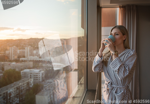 Image of young woman enjoying evening coffee by the window