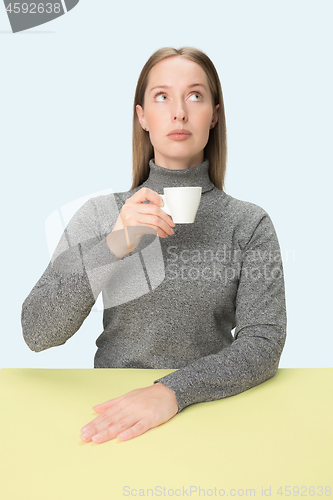 Image of Beautiful lonely woman sitting at studio and looking sad holding the cup of coffee in hand. Closeup toned portrait