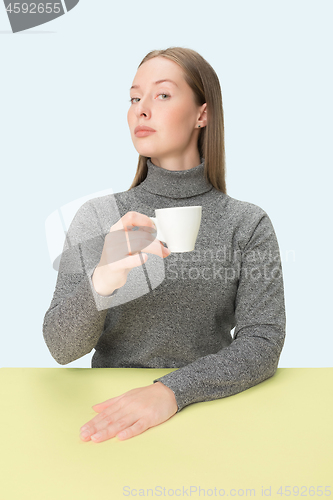 Image of Beautiful lonely woman sitting at studio and looking sad holding the cup of coffee in hand. Closeup toned portrait