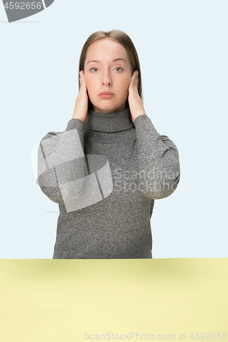 Image of portrait of stressed woman sitting at table with closed and covering her ears with hands.