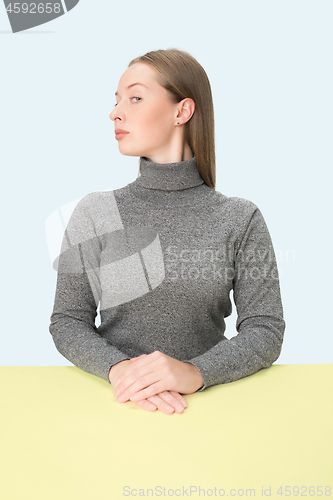 Image of Serious business woman sitting at a table on a pink background