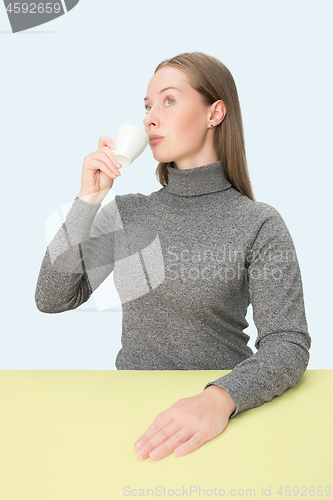 Image of Beautiful lonely woman sitting at studio and looking sad holding the cup of coffee in hand. Closeup toned portrait