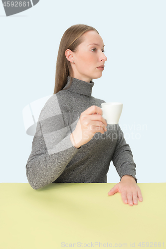 Image of Beautiful lonely woman sitting at studio and looking sad holding the cup of coffee in hand. Closeup toned portrait