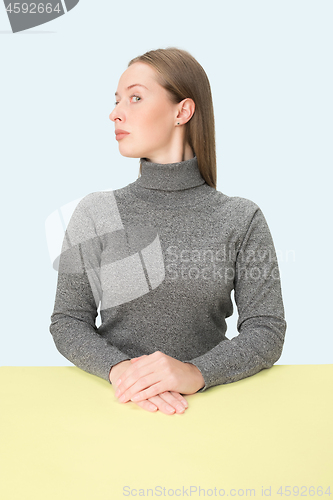 Image of Serious business woman sitting at a table on a pink background