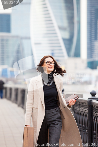 Image of attractive middle-aged woman in a light coat smiles