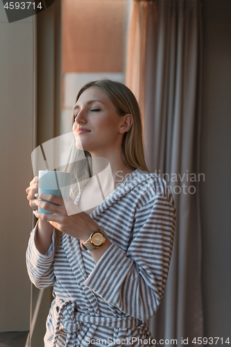 Image of young woman enjoying evening coffee by the window