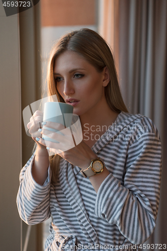 Image of young woman enjoying evening coffee by the window