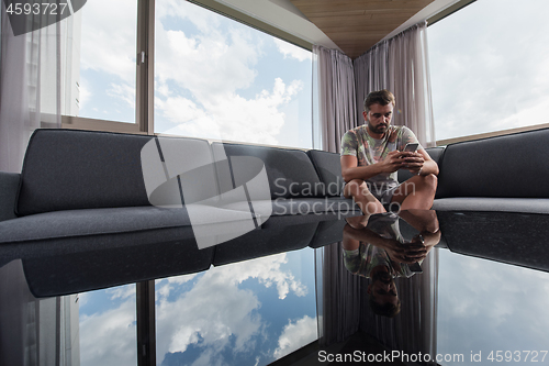 Image of young casual man using a mobile phone at home