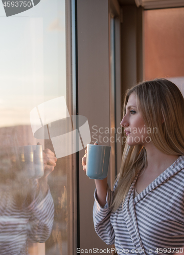 Image of young woman enjoying evening coffee by the window