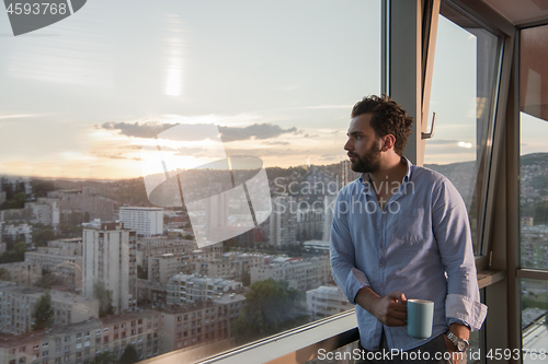 Image of young man enjoying evening coffee by the window