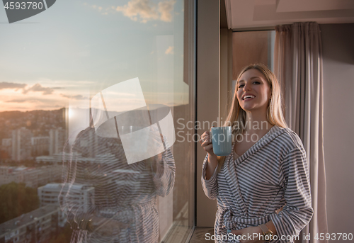 Image of young woman enjoying evening coffee by the window