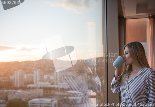 Image of young woman enjoying evening coffee by the window