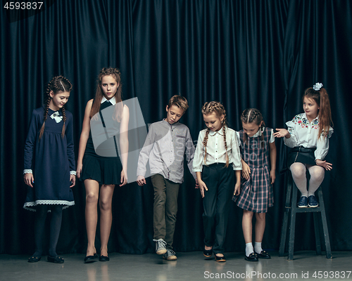 Image of Cute stylish children on dark studio background. The beautiful teen girls and boy standing together