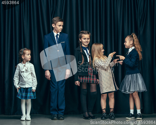 Image of Cute stylish children on dark studio background. The beautiful teen girls and boy standing together