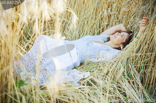 Image of beautiful woman in a white dress lies in the ears of corn
