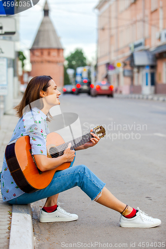 Image of Girl in a blue shirt and jeans with a guitar in the old town