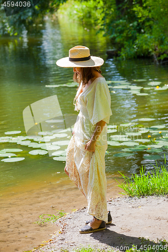 Image of woman in a straw hat and white summer dress on the shore of an o