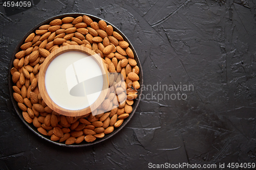 Image of Composition of almonds seeds and milk, placed on black stone background.