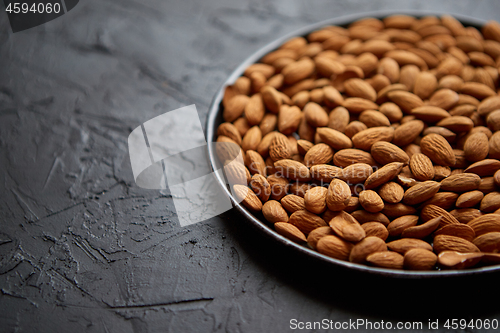 Image of Whole almond nuts in black plate placed on black stone table