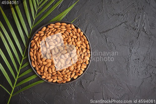 Image of Composition of Whole almond nuts in black plate placed on black stone table