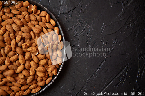 Image of Whole almond nuts in black plate placed on black stone table