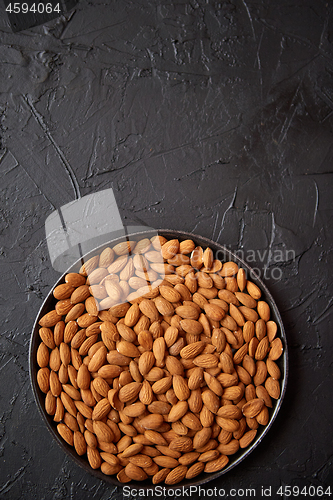 Image of Whole almond nuts in black plate placed on black stone table