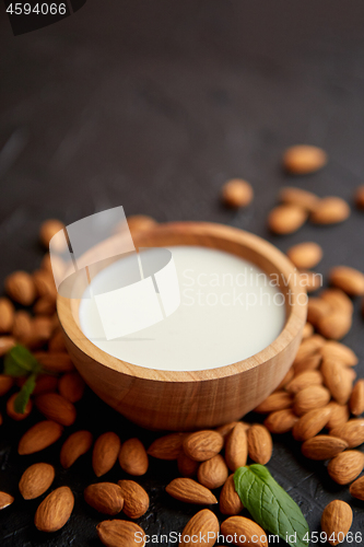 Image of Fresh almond milk in wooden bowl and almonds on black stone background