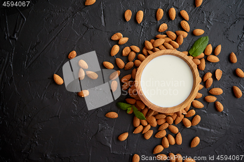 Image of Fresh almond milk in wooden bowl and almonds on black stone background