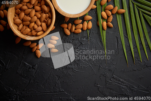 Image of Amond seeds in wooden bowl, fresh natural milk placed on black stone background