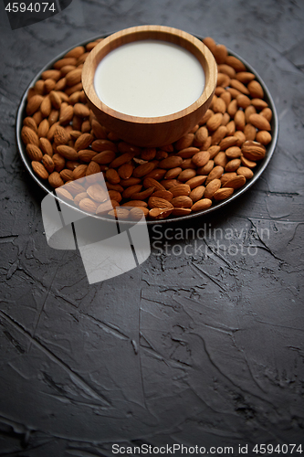 Image of Composition of almonds seeds and milk, placed on black stone background.