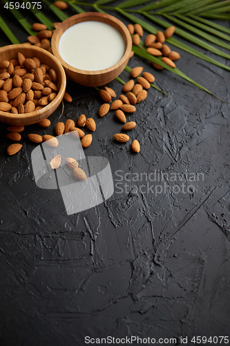 Image of Amond seeds in wooden bowl, fresh natural milk placed on black stone background