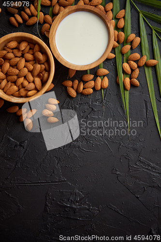 Image of Amond seeds in wooden bowl, fresh natural milk placed on black stone background