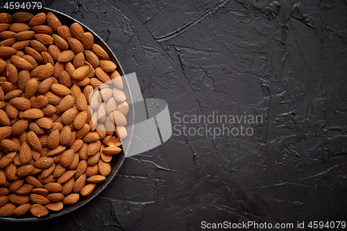 Image of Whole almond nuts in black plate placed on black stone table