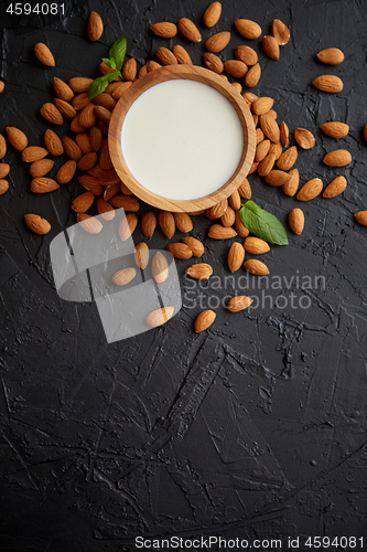 Image of Fresh almond milk in wooden bowl and almonds on black stone background