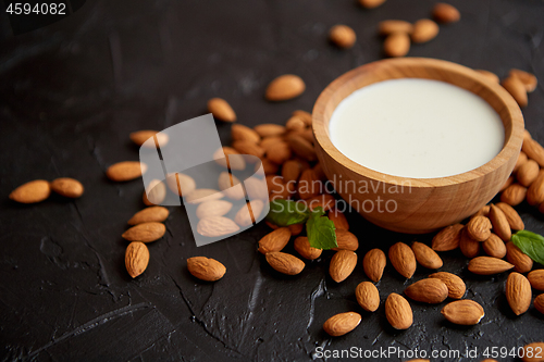 Image of Amond seeds with bowl of fresh natural milk placed on black stone background