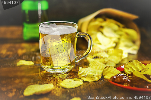 Image of A glass of cold beer and chips on a wooden table. The concept of