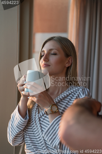 Image of young woman enjoying evening coffee by the window