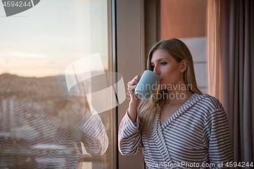 Image of young woman enjoying evening coffee by the window