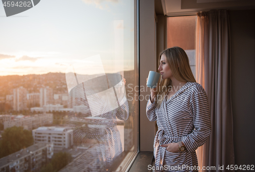 Image of young woman enjoying evening coffee by the window