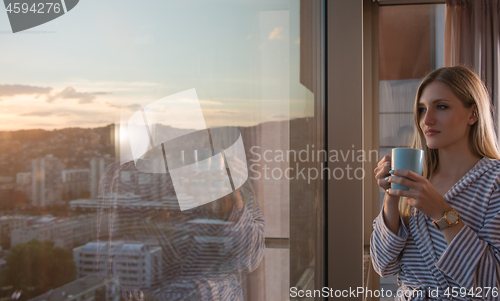 Image of young woman enjoying evening coffee by the window