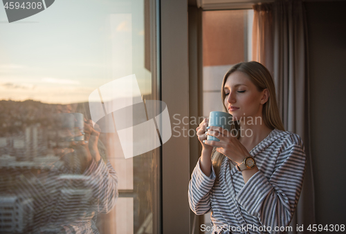 Image of young woman enjoying evening coffee by the window