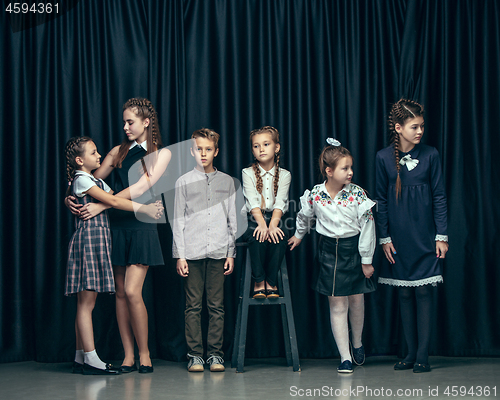 Image of Cute stylish children on dark studio background. The beautiful teen girls and boy standing together