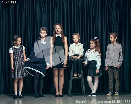 Image of Cute stylish children on dark studio background. The beautiful teen girls and boy standing together