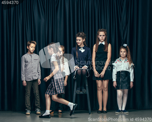 Image of Cute stylish children on dark studio background. The beautiful teen girls and boy standing together