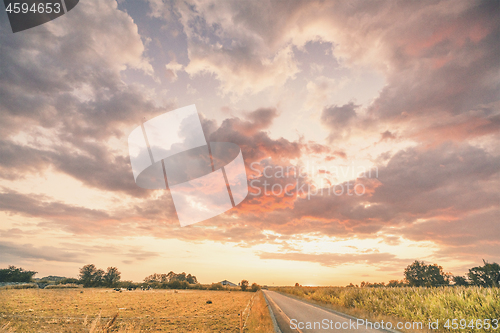 Image of Rural sunset with an asphalt road crossing a countryside