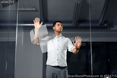 Image of businessman touching glass wall at night office